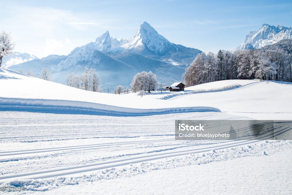 Beautiful winter wonderland mountain scenery in the Alps with cross country skiing track on a scenic cold sunny day with blue sky and clouds